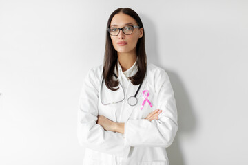Portrait of woman doctor with pink ribbon on white coat posing against white wall background. World Cancer Day concept