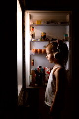 A girl in the headphones looking into the fridge
