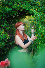 Obraz premium Stylish beautiful redhair woman poses amid vibrant garden foliage