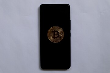 Smartphone with bitcoin display on black screen placed on gray paper