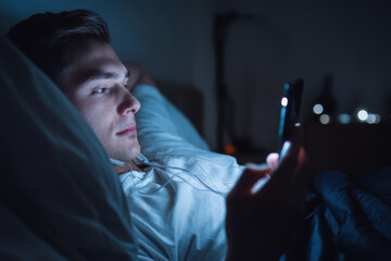 A sleepless man is lying in bed and doom scrolling on cellphone during bedtime