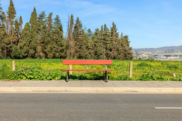 Red bench inviting to relax by the road with trees and airplanes in background