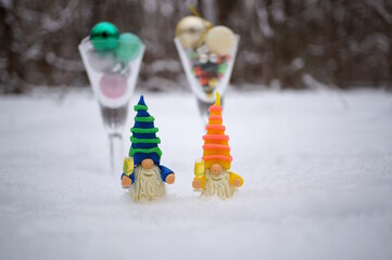 Two dwarfs with glasses of champagne in a snowy forest. Next to it are two glasses with Christmas tree toys. New Year and Christmas.
