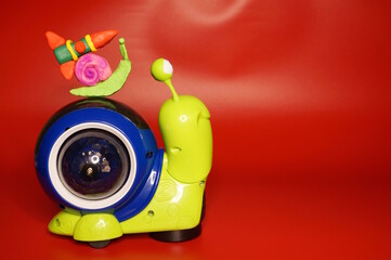 A snail with a plasticine rocket is on another toy snail. Red background.