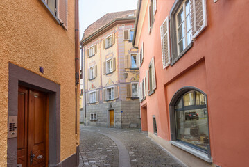 Fototapeta premium Narrow cobblestone street lined with traditional colourful buildings and shops in Chur, Switzerland, at sunset in spring
