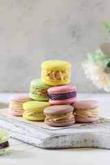 Colorful macarons stacked on a decorative board surrounded by flowers in a bright setting