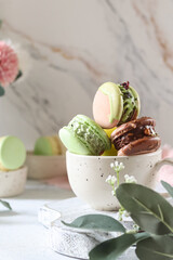 Colorful macarons stacked in a bowl on a marble surface with floral accents