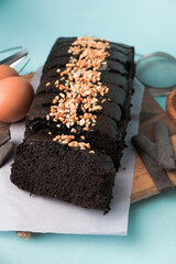 Chocolate brownie on a wooden board with egg and cake ingredients on blue background