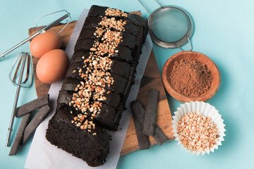 Chocolate brownie on a wooden board with egg and cake ingredients on blue background