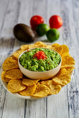fresh guacamole topped with tomato salsa served with tortilla strips, on a white platter