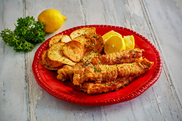 crispy fried fish fillets served with homemade seasoned potato chips on a red plate
