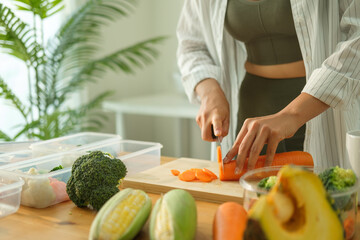 Close up of woman preparing healthy meals on kitchen counter surrounded by fresh ingredients and storage containers.