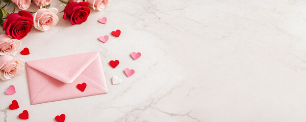 Letter envelope with paper hearts on a light marble table with roses. Valentine's Day, wedding or anniversary background for poster or banner with copy space. Romantic and love concept.