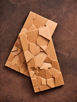 A distinctive chocolate bar rests on a rich, dark surface, showcasing an intricate, cracked design. The contrasting colors emphasize the artisanal quality and appeal