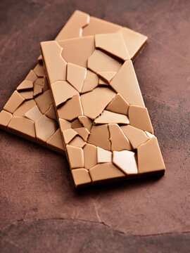 Two elegant pieces of broken chocolate are displayed on a rich brown surface, illustrating the craftsmanship of artisan chocolates and their intricate design