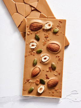 A caramel chocolate bar is topped with almonds, hazelnuts, and pumpkin seeds, creating a tempting and textured treat. Perfect for dessert or snacking anytime