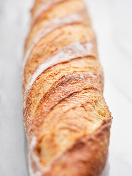 A long, crusty bread loaf displays a beautiful golden exterior with a soft inner texture. It is placed on a clean countertop, emphasizing its artisanal quality