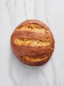 A perfectly crafted round loaf of sourdough bread sits on a clean marble surface, showcasing its crusty exterior and rustic design. The warm tones evoke a homemade quality