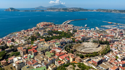 Aerial view of the Flavian Amphitheater, located in the historic center of Pozzuoli, near Naples, Italy. In the background are the Tyrrhenian Sea, the promontory of Capo Miseno and Ischia island.