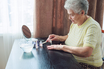 Elderly woman in her 70s giving herself a manicure at home, symbolizing self-care, beauty, and...
