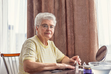 Elderly woman with gray hair wearing glasses 70+ years old doing her own manicure at home, Self-care theme, beauty and self-care, self-love, independence and aging with grace