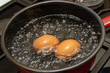 Two orange eggs boiling in a  black pot with bubbles and steam, soft focus  close up