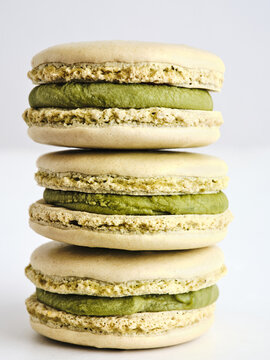 Four delectable macarons filled with smooth matcha cream are stacked appealingly against a plain background. Their unique color and texture invite a delightful tasting experience