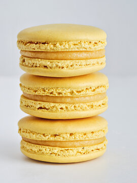 Three beautifully crafted yellow macarons are stacked neatly on a white surface. Each macaron features a smooth, glossy shell with a creamy filling, showcasing gourmet dessert artistry