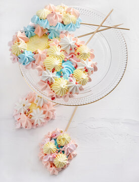 Delicate meringue pops in pastel colors are artfully displayed on a clear glass plate. These sweet treats add a festive touch to any celebration with their vibrant design and playful shapes