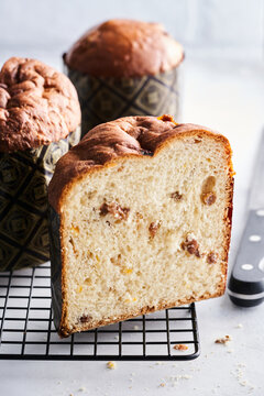 Delicious sweet bread loaf is sliced, showcasing a soft, light texture with chunks of dried fruits and nuts. It is placed on a wire rack, ready for serving