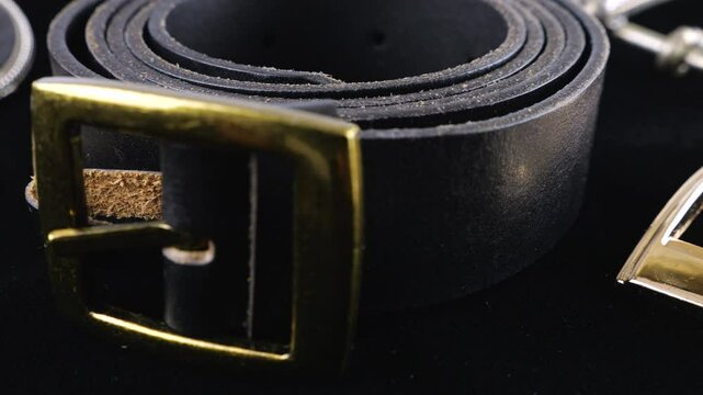 Black genuines leather belts and buckles of different designs rotate on black velvet background.