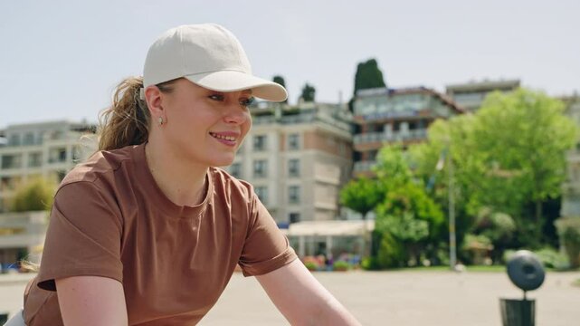 Woman rides rental bicycle on Buyukada Island, enjoys cityscape. Female cyclist explores sunny urban area, smiles during activity. Leisure ride, outdoor sport in scenic Istanbul background.