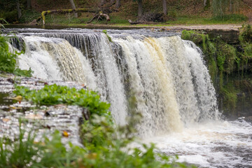 
A waterfall with several cascading waterfalls falling over a rocky surface surrounded by green...