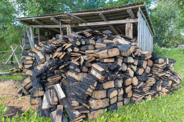 
A pile of dead firewood logs near a shed on a farm.