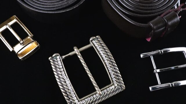 Black genuines leather belts and buckles of different designs rotate on black velvet background.
