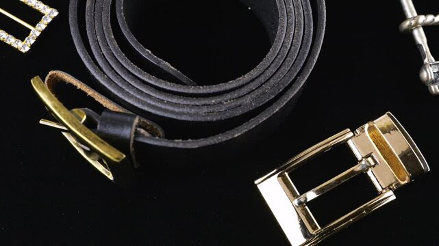 Black genuine leather belt and buckles of different designs rotate on black velvet background.