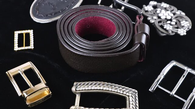 Black genuine leather belt and buckles of different designs rotate on black velvet background.