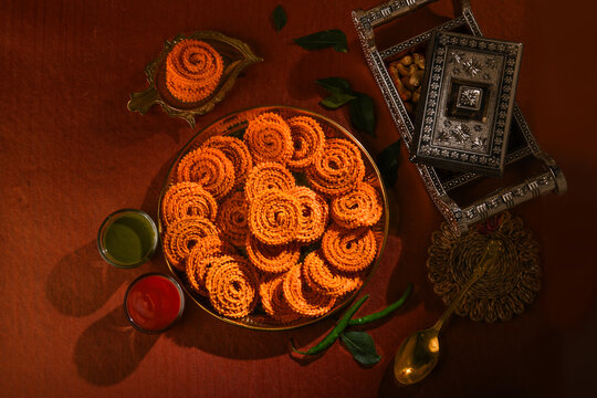 A black bean on a brown and natural background with Maharashtrian food Chakli on it along with curry leaves, green chutney, red chutney sauce It is specially made during the festival of Diwali.