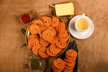 chakli arranged on golden plate dish with tea,cheese with tomato sous raw cloth backround
