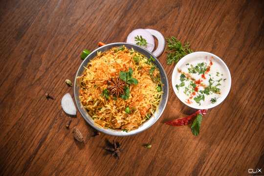 veg biryani in handi with garnish & raita bowl on wooden table background