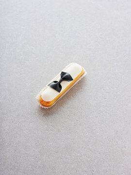 An elegant pastry styled with a black bow tie design sits on a soft gray surface. This delightful treat showcases intricate attention to detail and artistic flair