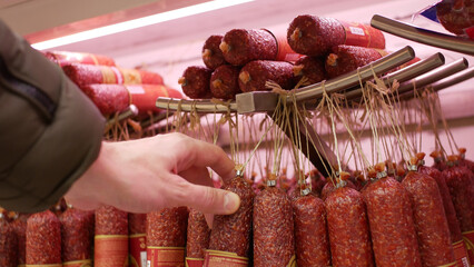 A male customer's hand taking a sausage in a meat department