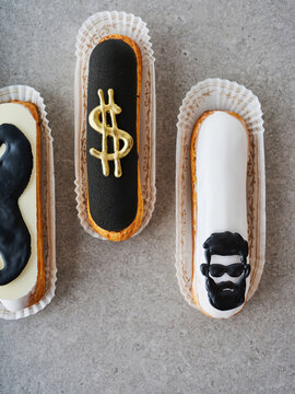 A tray features three elegant pastries, each uniquely decorated with black and white icing, showcasing creative designs like a dollar sign and a face