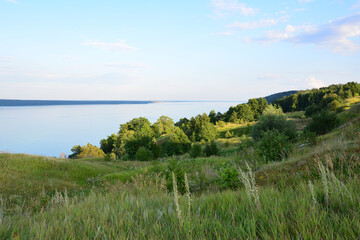 Obraz premium a green hill with some trees and a lake and sunset sky in the background