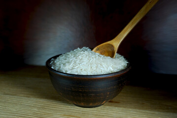bowl of white long grain rice and wooden spoon on dark background