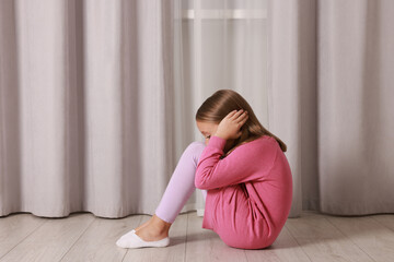 Autism concept. Scared little girl covering her ears on floor at home