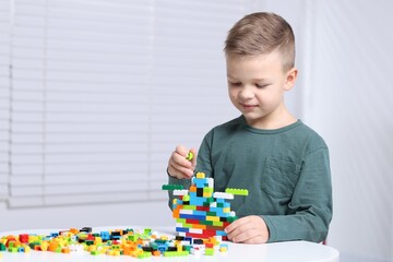 Fototapeta premium Cute boy playing with building blocks at white table indoors. Space for text