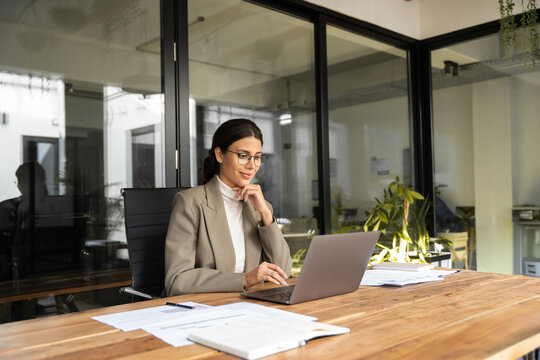 Young professional it specialist latin hispanic business lady working on laptop pc sitting at desk in modern office space. 30s middle eastern indian woman using computer technology app for work online