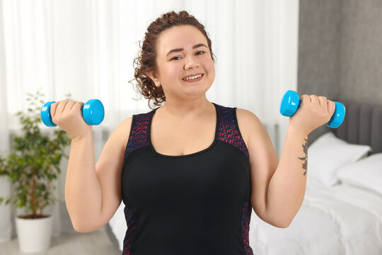 Plus size woman with dumbbells training at home