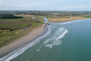A sweeping aerial view of Ballynamona Strand Beach in Ireland, showcasing its expansive sandy shoreline, gentle waves, and lush coastal surroundings from above.
